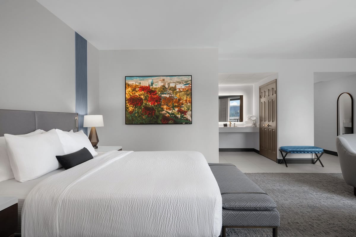 A hotel room with a large bed, a desk, a chair, and a painting on the wall.