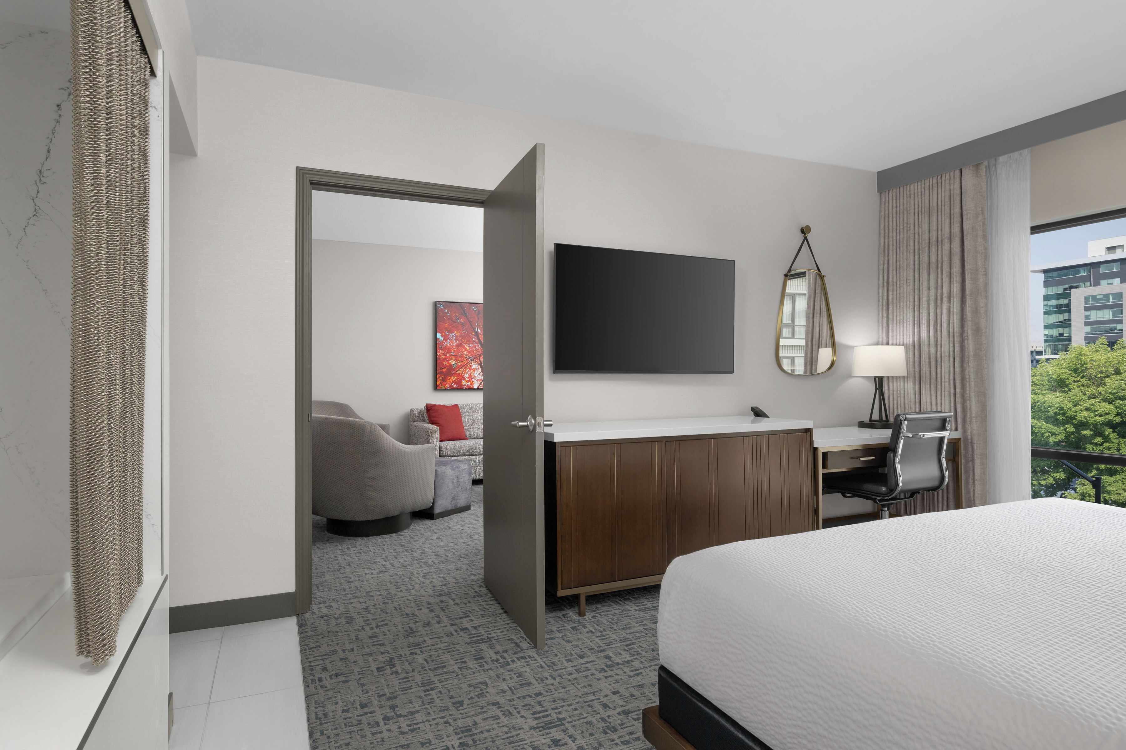A hotel room with a bed, a desk, a chair, a TV, and a view of the city.