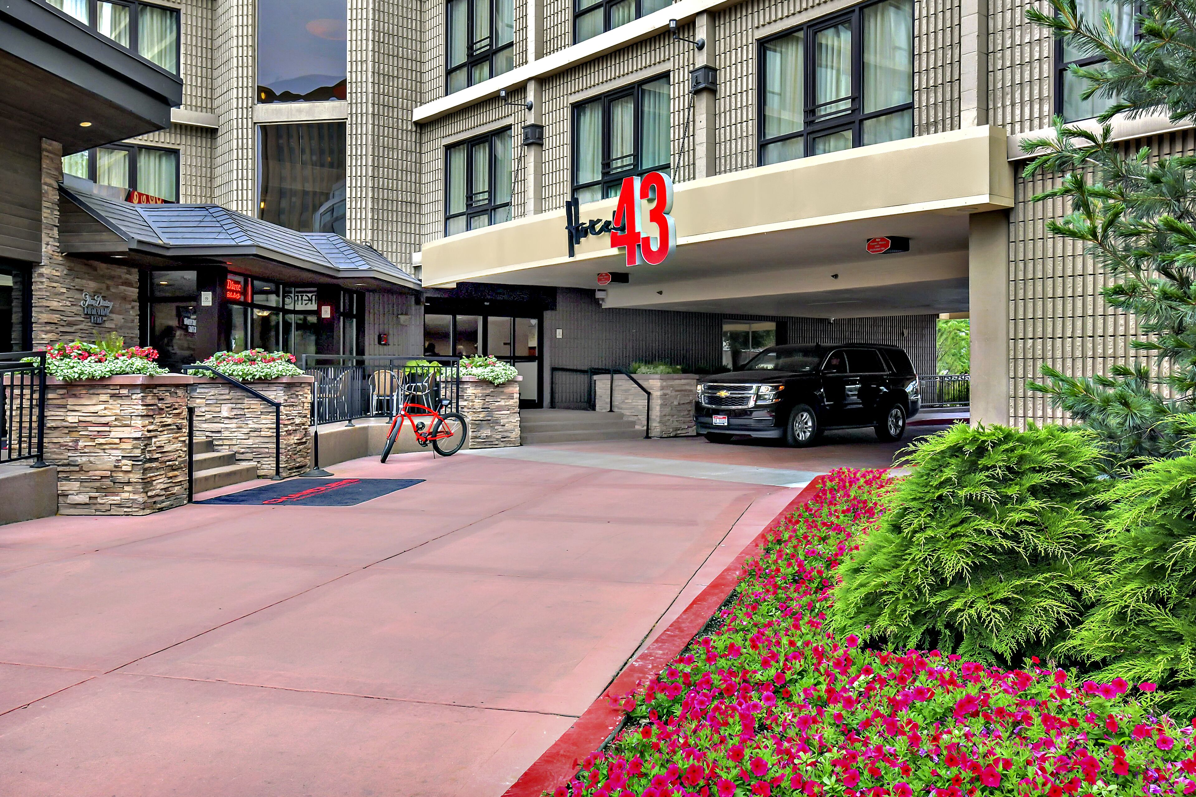 A hotel entrance with a number '43' sign, a bike parked outside, and a car parked in the driveway.