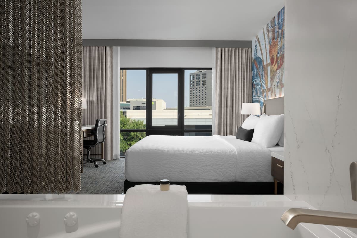 A modern hotel room with a large bed, a desk, and a view of the cityscape.