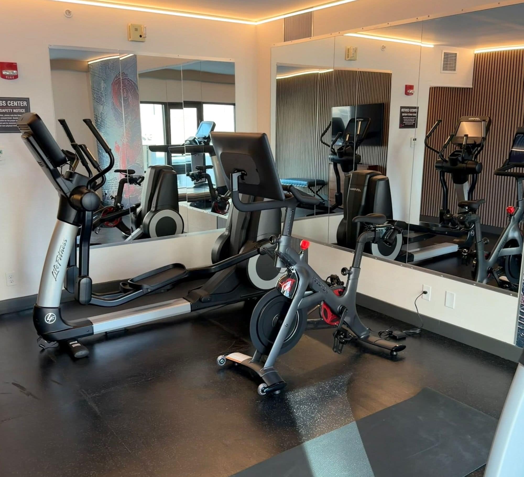 A gym with cardio equipment, a mirrored wall, and a safety notice.