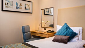 A hotel room with a bed, a desk, a chair, a mirror, and framed artwork on the wall. - Thistle Euston (London)