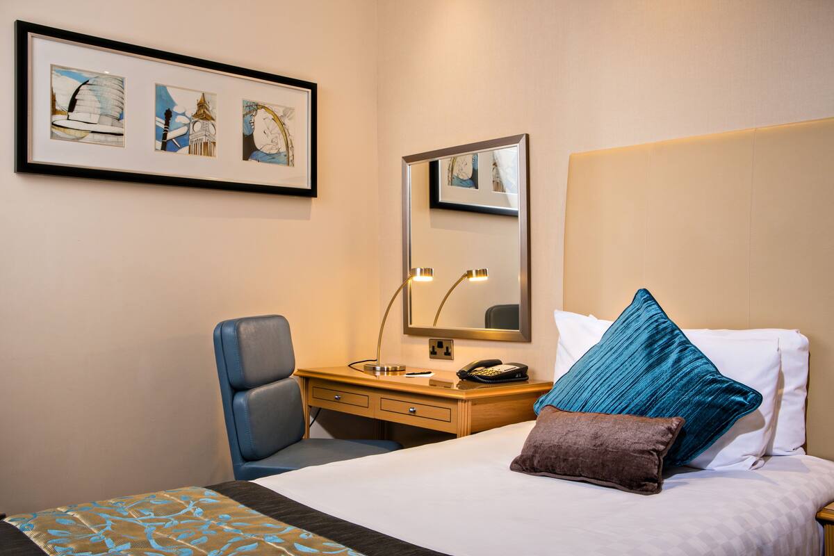 A hotel room with a bed, a desk, a chair, a mirror, and framed artwork on the wall.