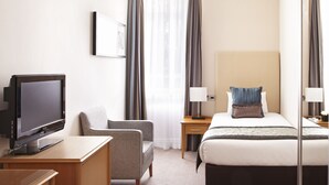 A hotel room with a bed, a desk with a TV, a chair, a bedside table with a lamp, and a large mirror. - Thistle Euston (London)