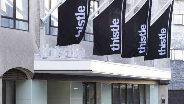 A building with multiple black flags with the word "thistle" on them, a modern facade, and large windows. - Thistle Euston (London)