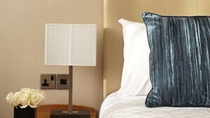 A neatly made bed with a headboard, a bedside table with a lamp, a vase of flowers, and a nightstand with a drawer. - Thistle Euston (London)