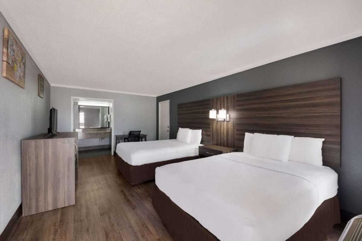 A hotel room with two beds, a desk, a chair, and a large mirror.