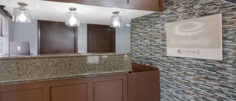 A hotel reception area with a granite counter, three pendant lights, a wall-mounted sign, and a patterned wall.