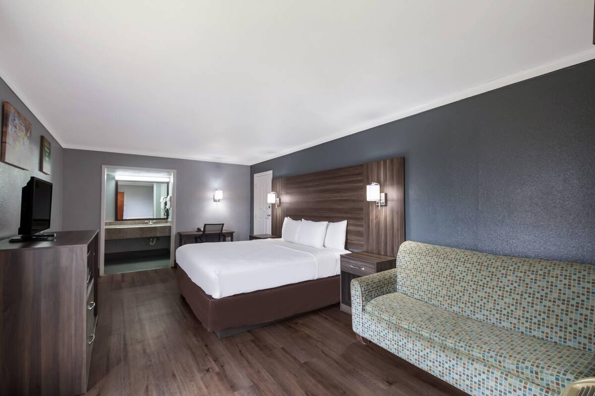A hotel room with a large bed, a desk, a chair, a TV, a mirror, and a sofa.