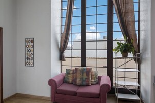 A room with a purple sofa, a potted plant, and a window with curtains.