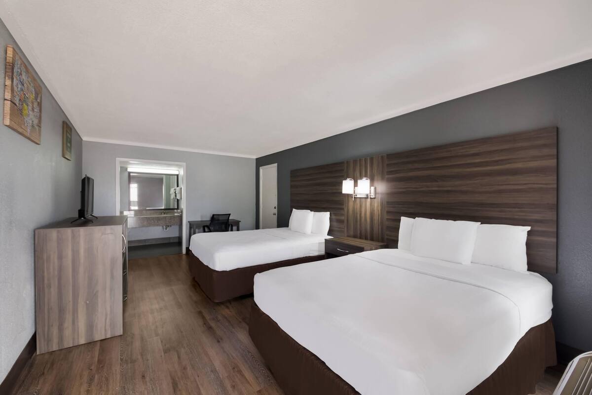 A hotel room with two beds, a desk, a chair, a mirror, and a wooden headboard.