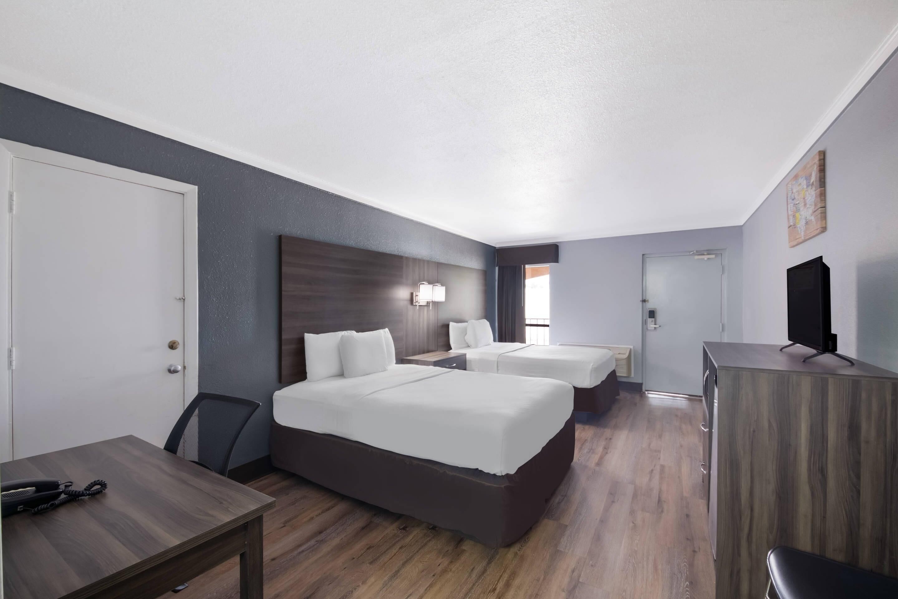 Una habitación de hotel con dos camas, un escritorio, una silla, un televisor y un armario.