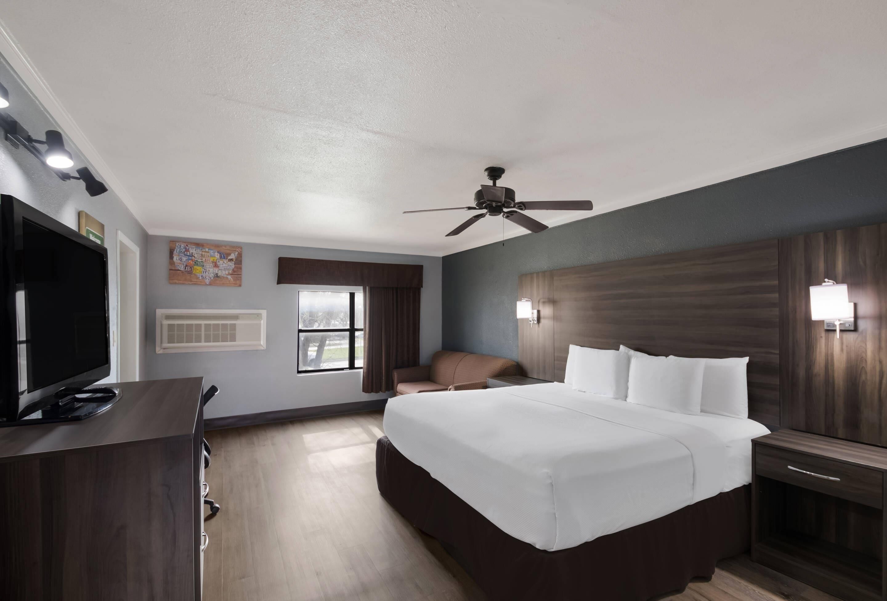 A hotel room with a large bed, a TV, a ceiling fan, a desk, and a window with curtains.