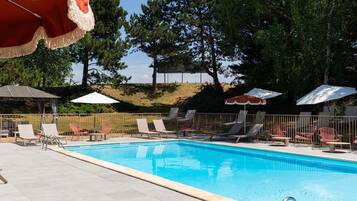 A swimming pool with lounge chairs and umbrellas, surrounded by trees and a hilly landscape.