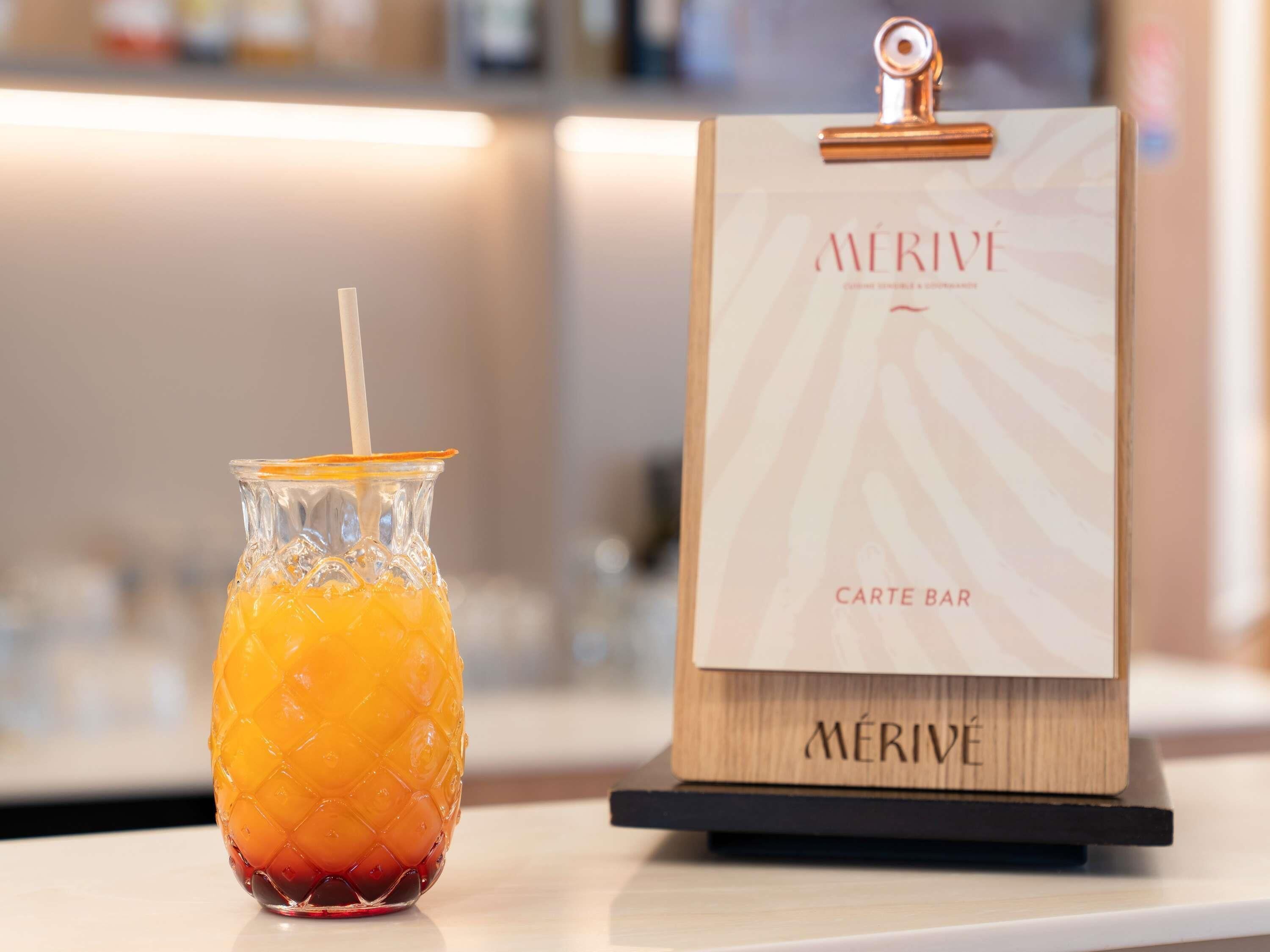 Un vaso con pajita y un cartel de madera con la palabra 'MÉRIVE' y 'CARTE BAR' escritas.