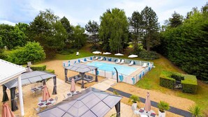 Un área de piscina con sillones reclinables, una zona de estar cubierta y una terraza con mesas y sombrillas.