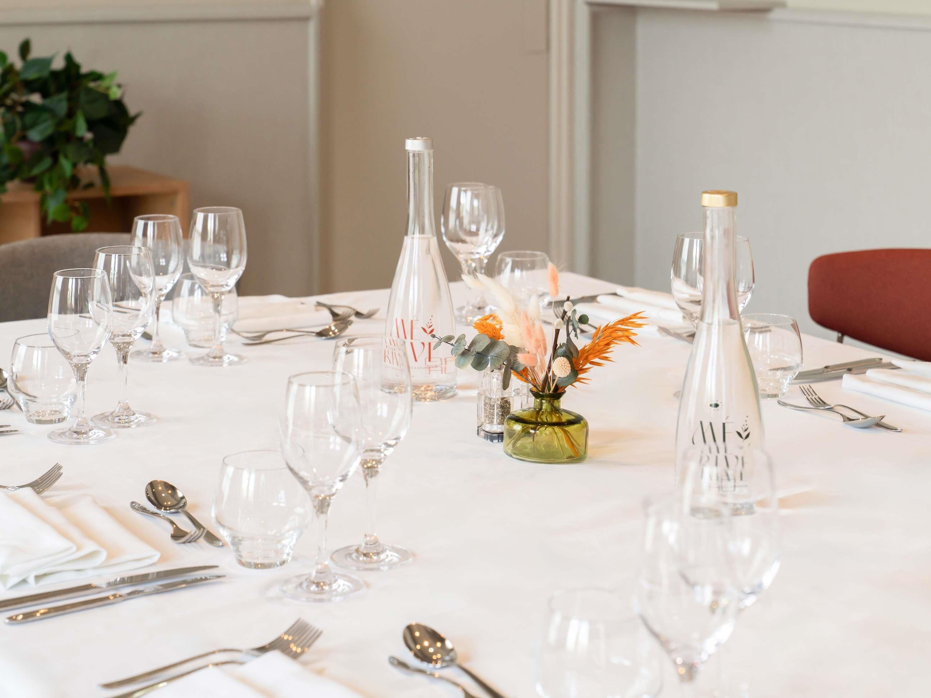 A table set for a meal with multiple wine glasses, a bottle of water, and a small vase with decorative flowers.