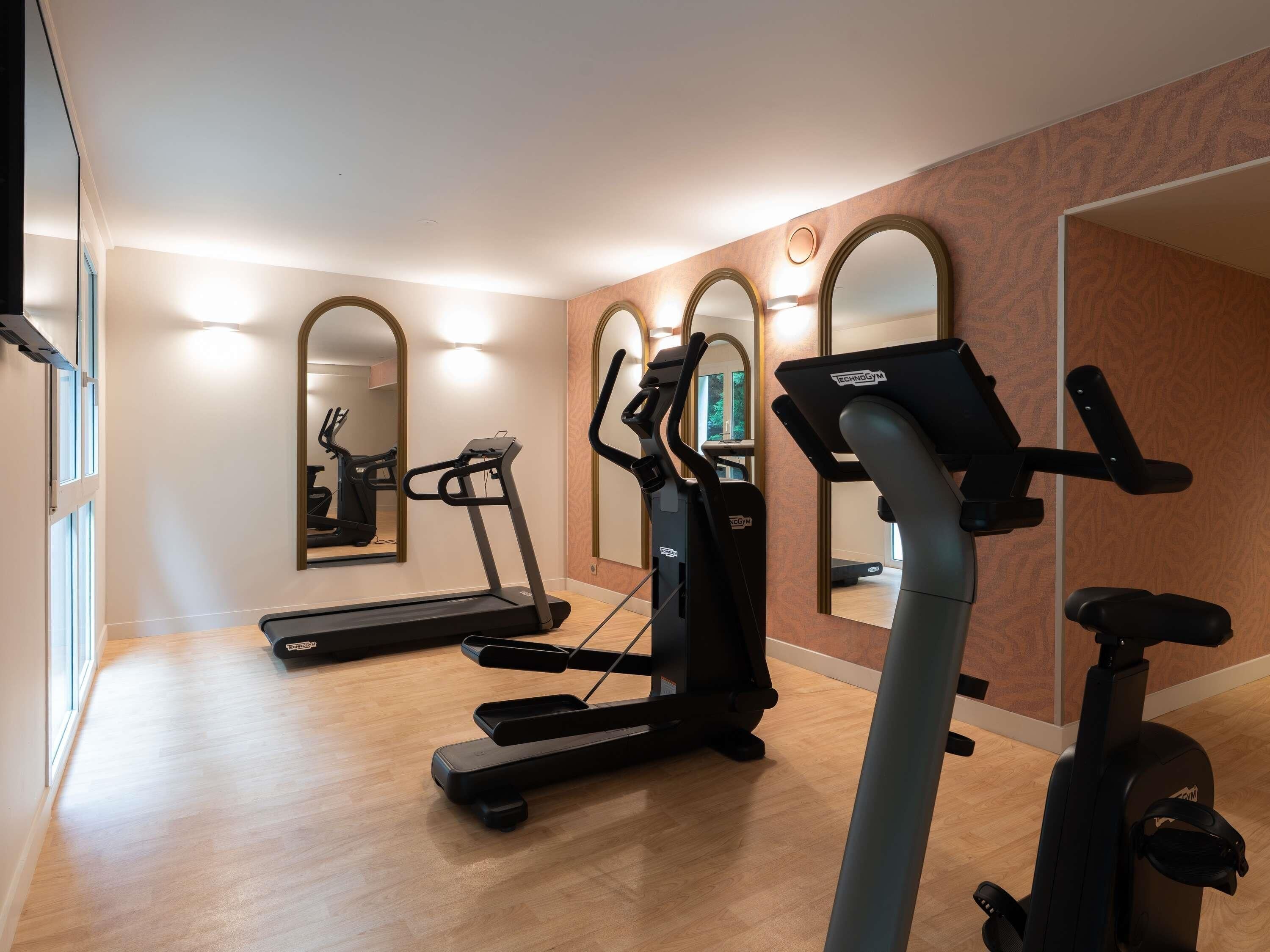 Un gimnasio con cintas de correr, elípticas y un muro de espejos.