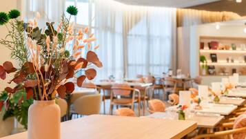 Een restaurant met een houten tafel en stoelen, een vaas met bloemen, en een licht interieur.