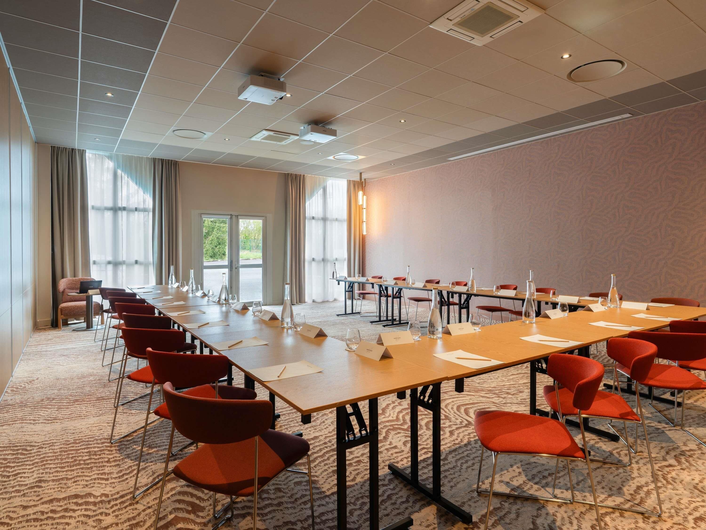 A conference room with a long table, red chairs, name cards, and a patterned carpet.
