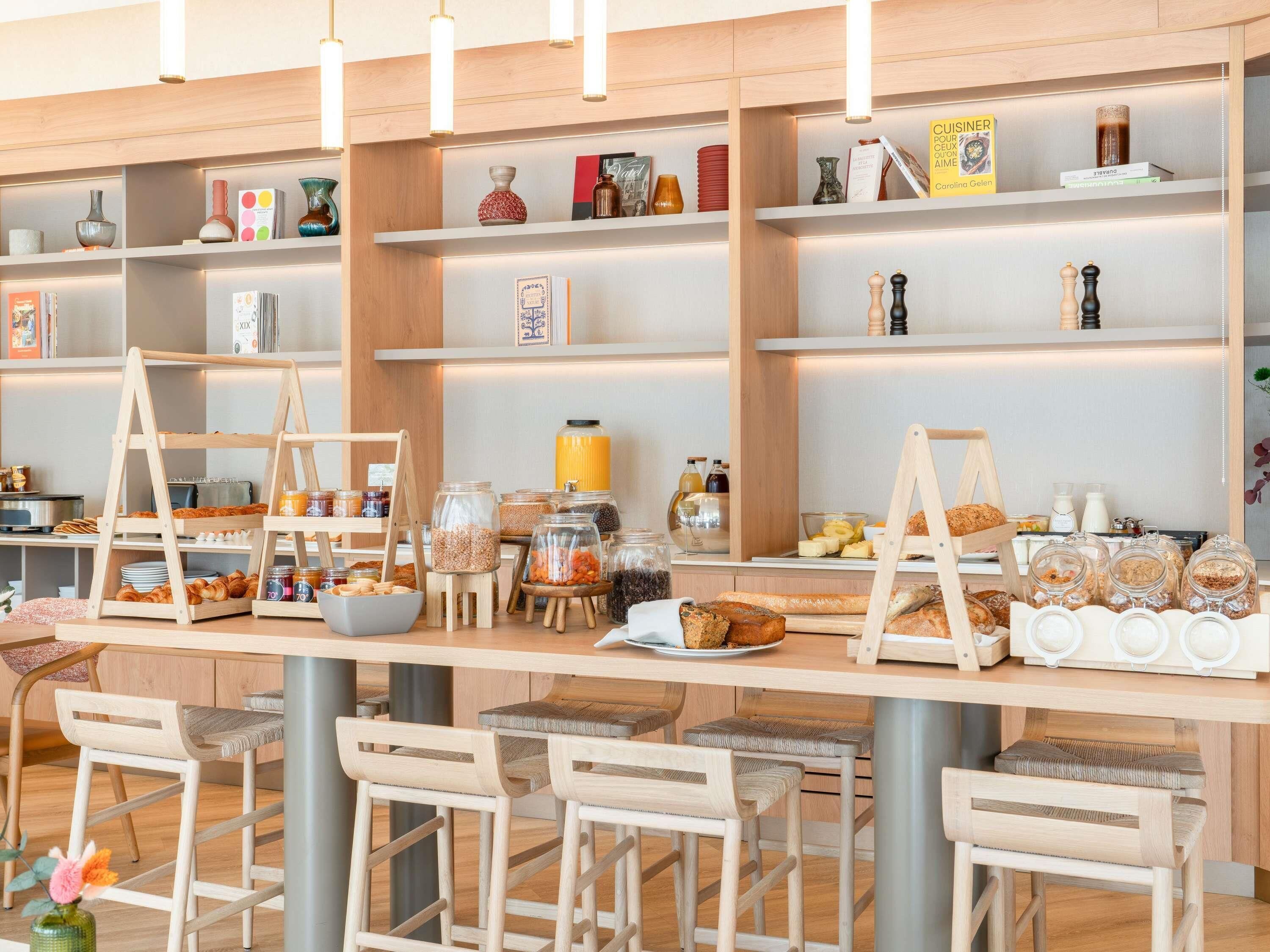 A café with wooden furniture, shelves with books and jars, and a variety of food items displayed.