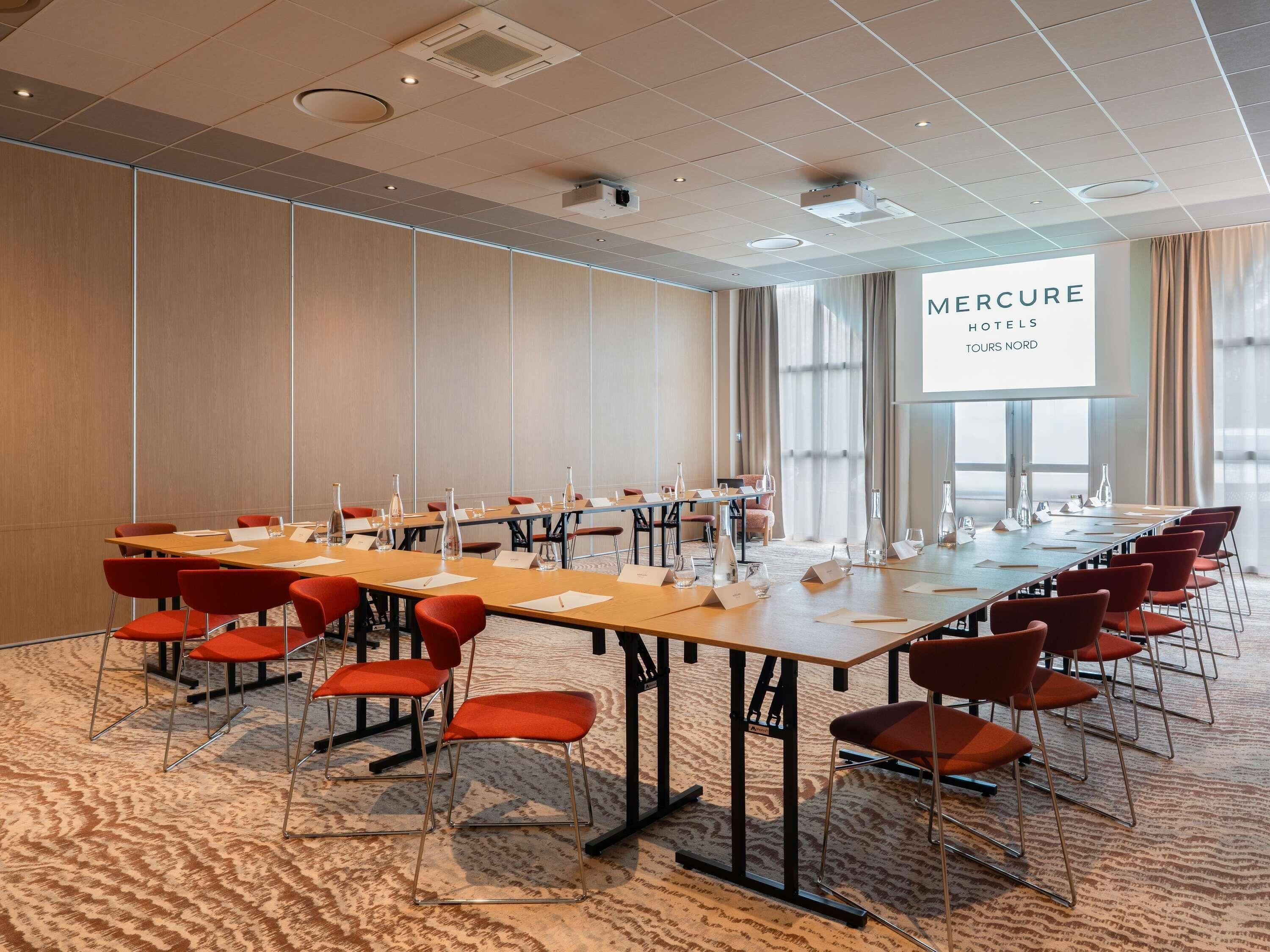 A conference room with multiple tables and chairs, a large projection screen, and a carpeted floor.