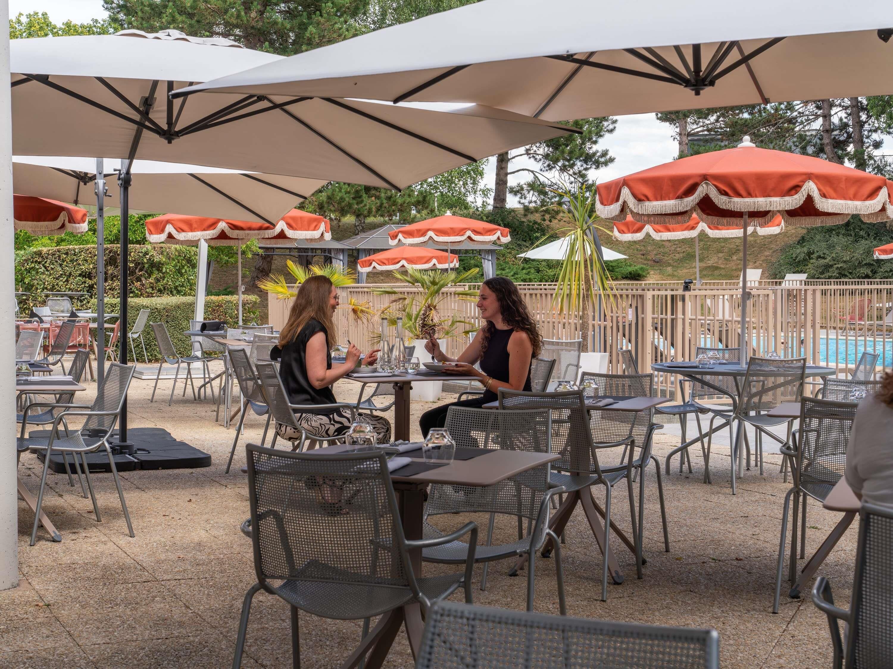 Un espace extérieur aménagé en terrasse, avec des tables et des chaises, dont certaines sont protégées par des parasols.