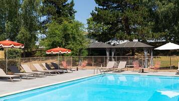 Une piscine entourée d’arbres, avec des chaises longues et des parasols.