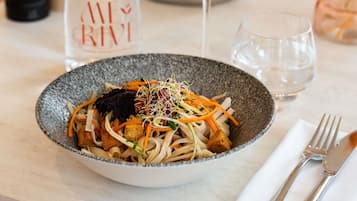 A bowl of noodle dish with vegetables and sprouts, a wine glass, and a water glass on a table.