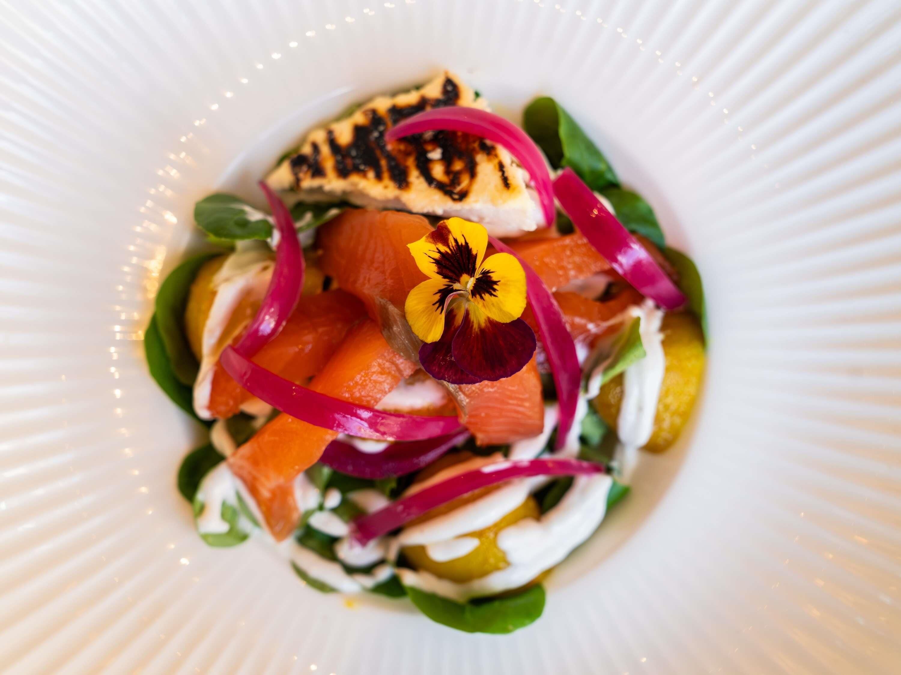 Un piatto con un'insalata, con verdure a foglia verde, carote e un fiore.