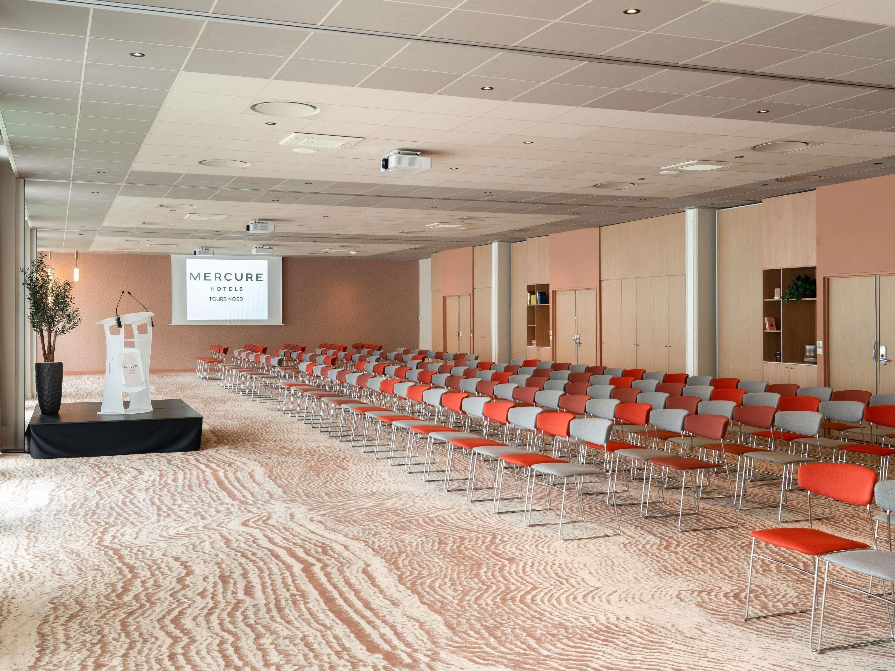 A conference room with rows of chairs, a podium, and a projection screen displaying 'Mercure Hotels Tours Nord'.
