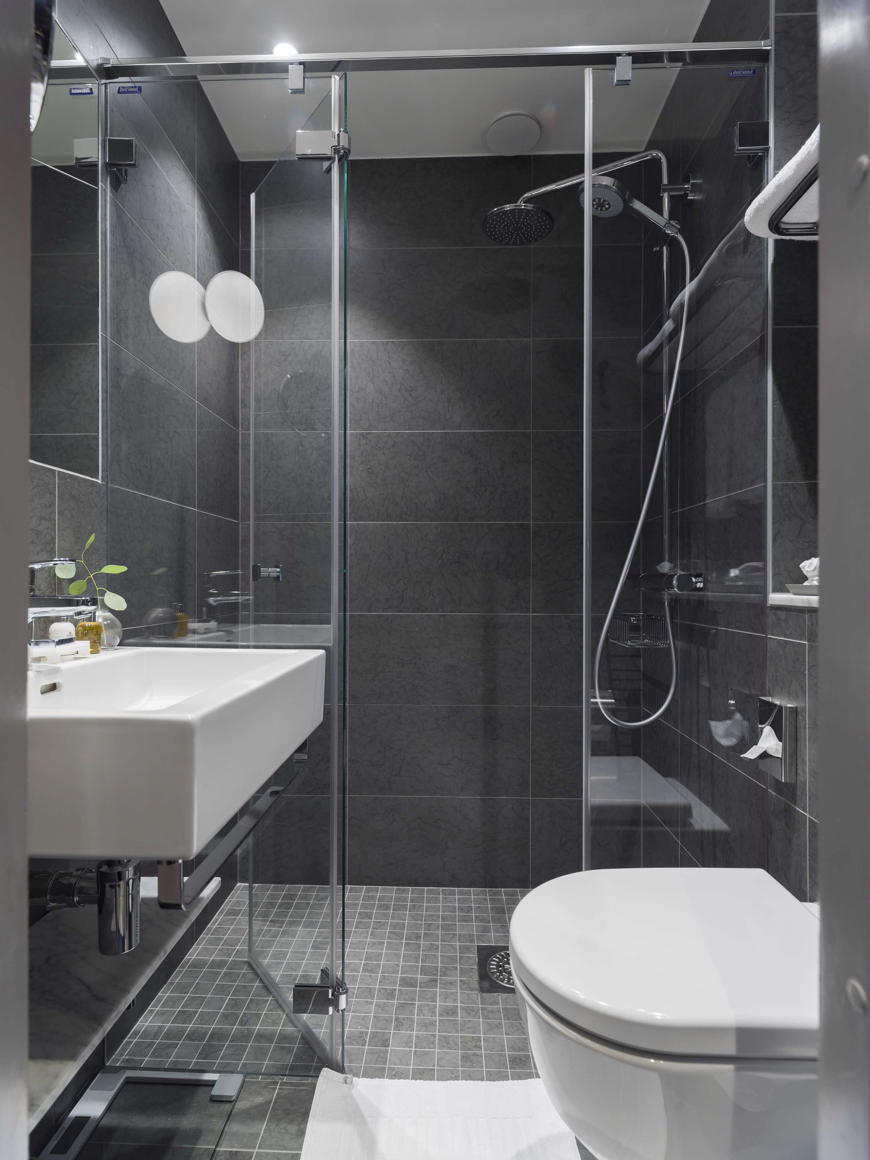 Un baño moderno con ducha de vidrio, lavamanos blanco y retrete.