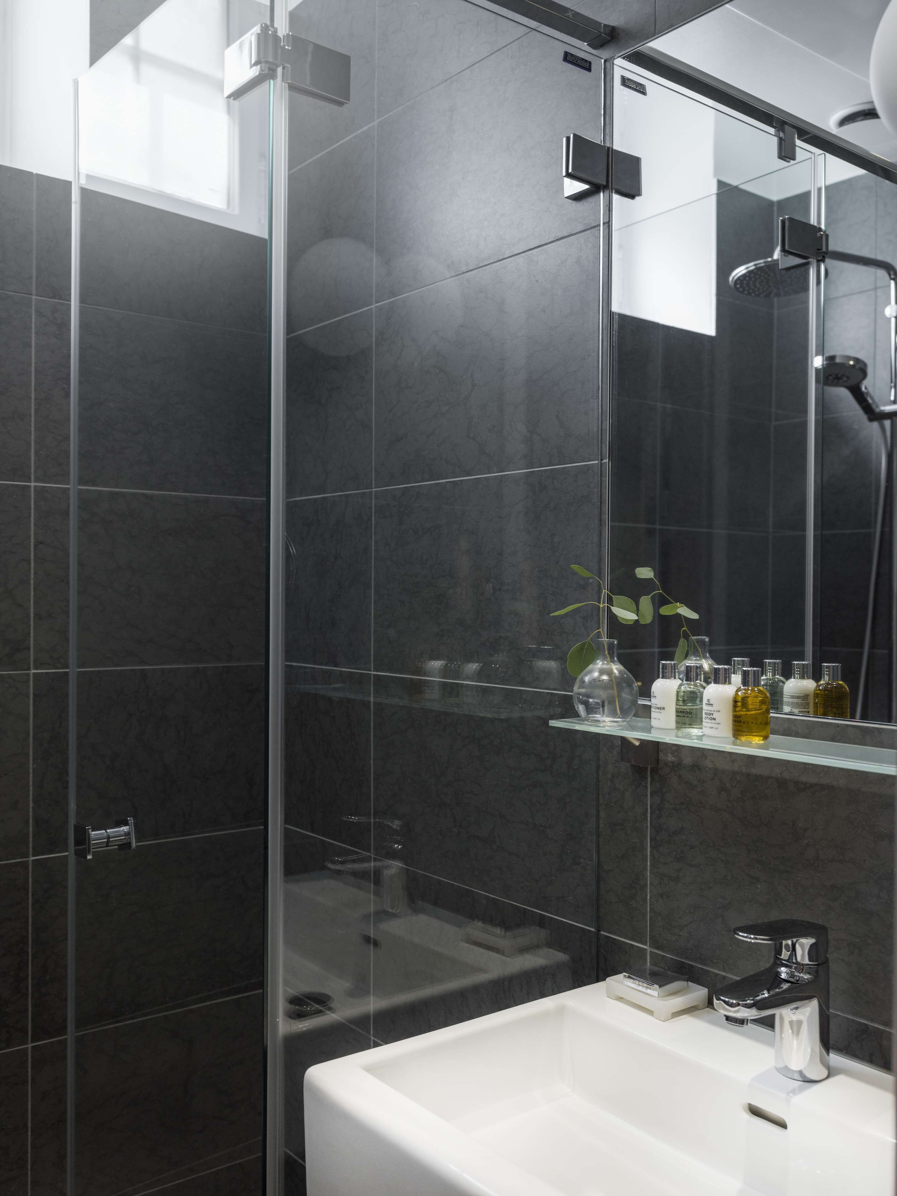 A modern bathroom with a glass shower enclosure, a white sink, and a mirror.