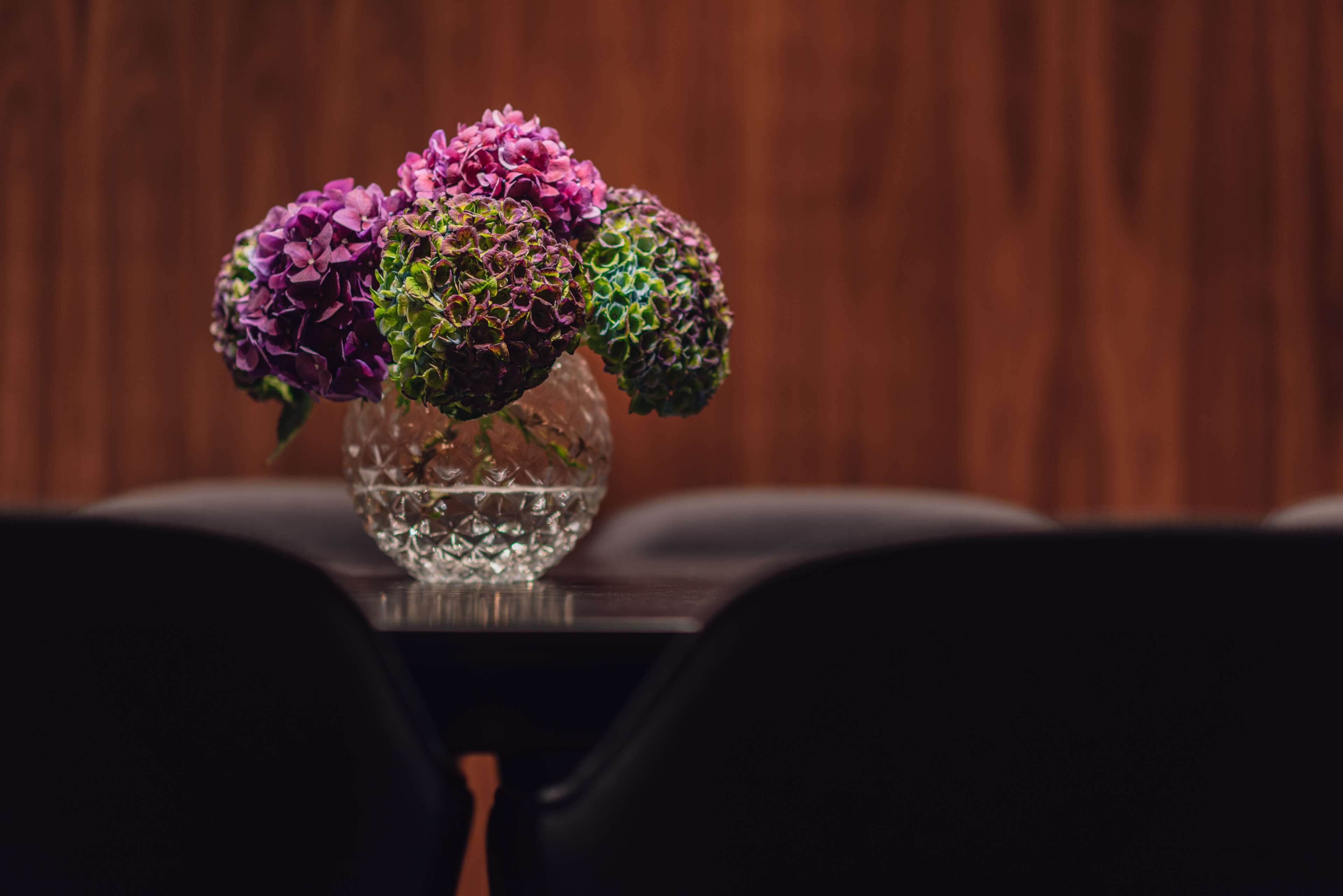 En genomskinlig glasvas med vatten och blommor står på ett bord.