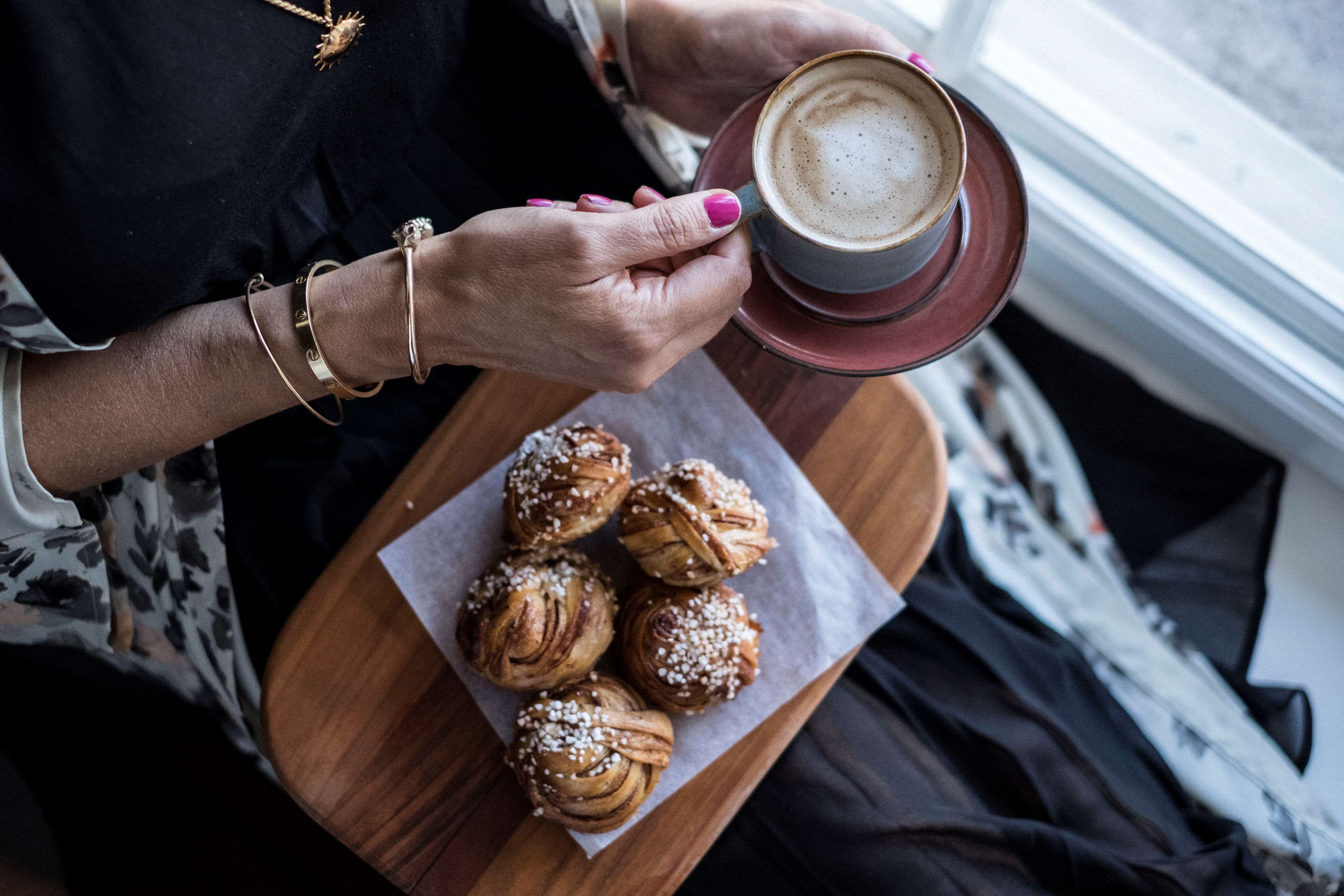 Uma pessoa segurando uma xícara de café e um prato de doces.
