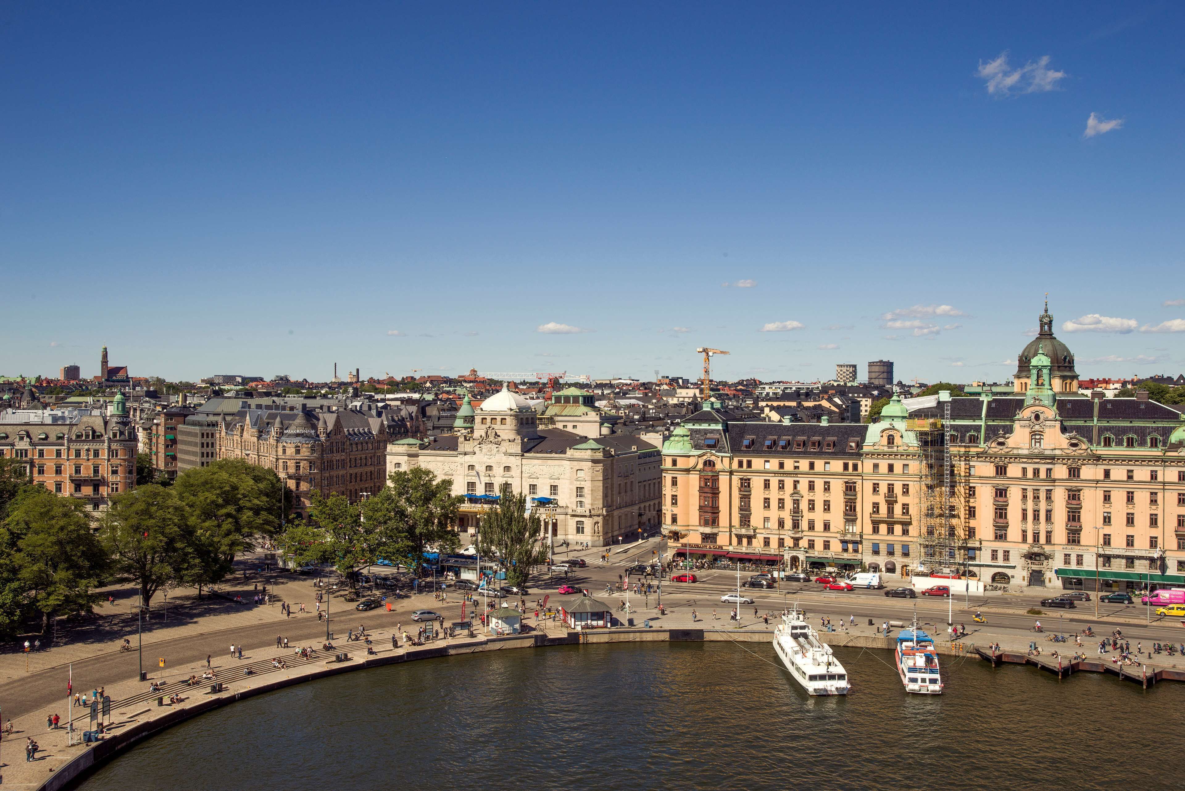 A waterfront cityscape with historic buildings, a large green dome, and a busy harbor with boats.