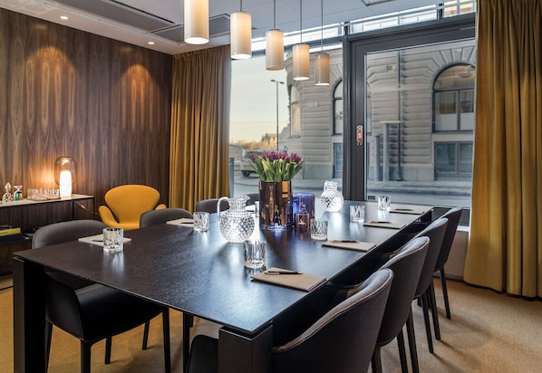 A conference room with a long table, chairs, a vase with flowers, and a view of a building through large windows.