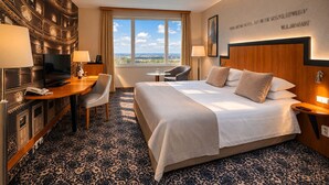 Camera d'albergo con un letto grande, una scrivania con la TV, una sedia, un tavolino e vista sulla città dalla finestra.