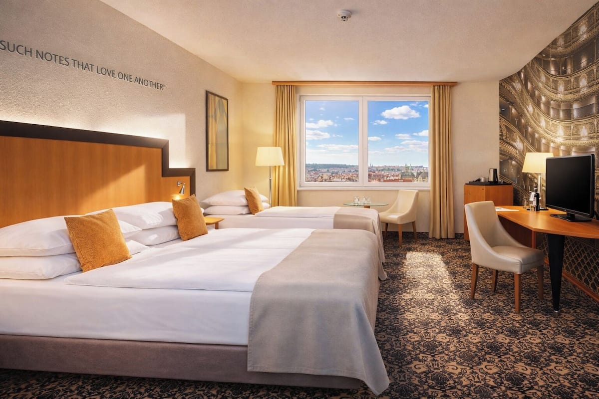 A hotel room with two beds, a desk, a chair, a television, and a city view.