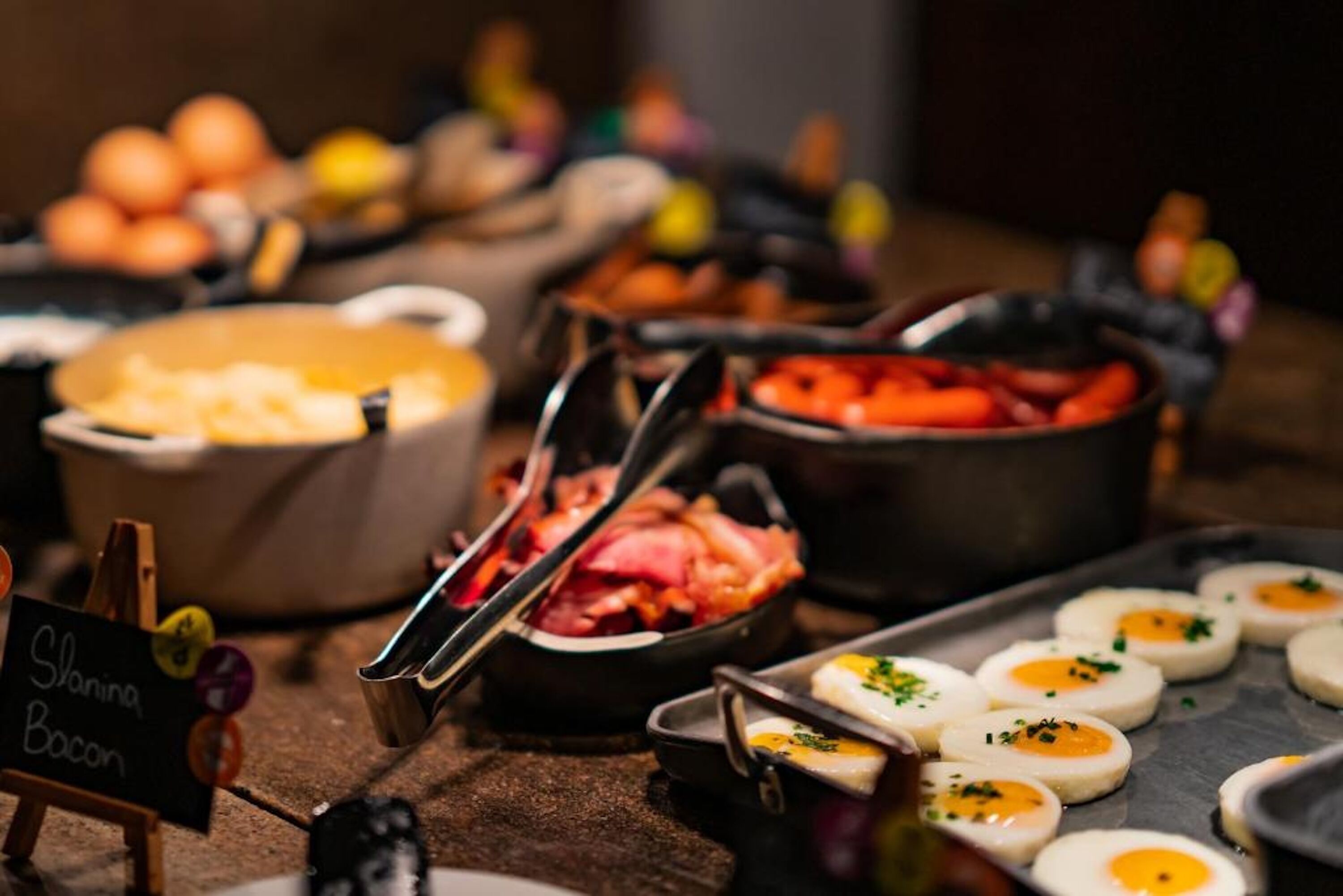 Un bufé con diferentes opciones de comida, incluyendo tocino, huevos y verduras.