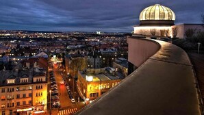 Paesaggio urbano al crepuscolo con una cupola imponente su una collina che domina una zona densamente popolata, con edifici e strade illuminate.