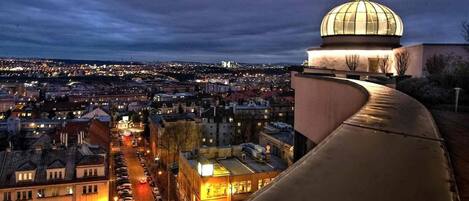 A cityscape at dusk with a prominent dome structure on a hill overlooking a densely populated area with illuminated buildings and streets.
