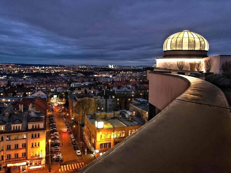 A cityscape at dusk with a prominent dome structure on a hill overlooking a densely populated area with illuminated buildings and streets.