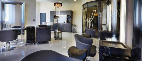 Un moderno salón de belleza con una recepción central, varias áreas de espera y una cocina a la vista.
