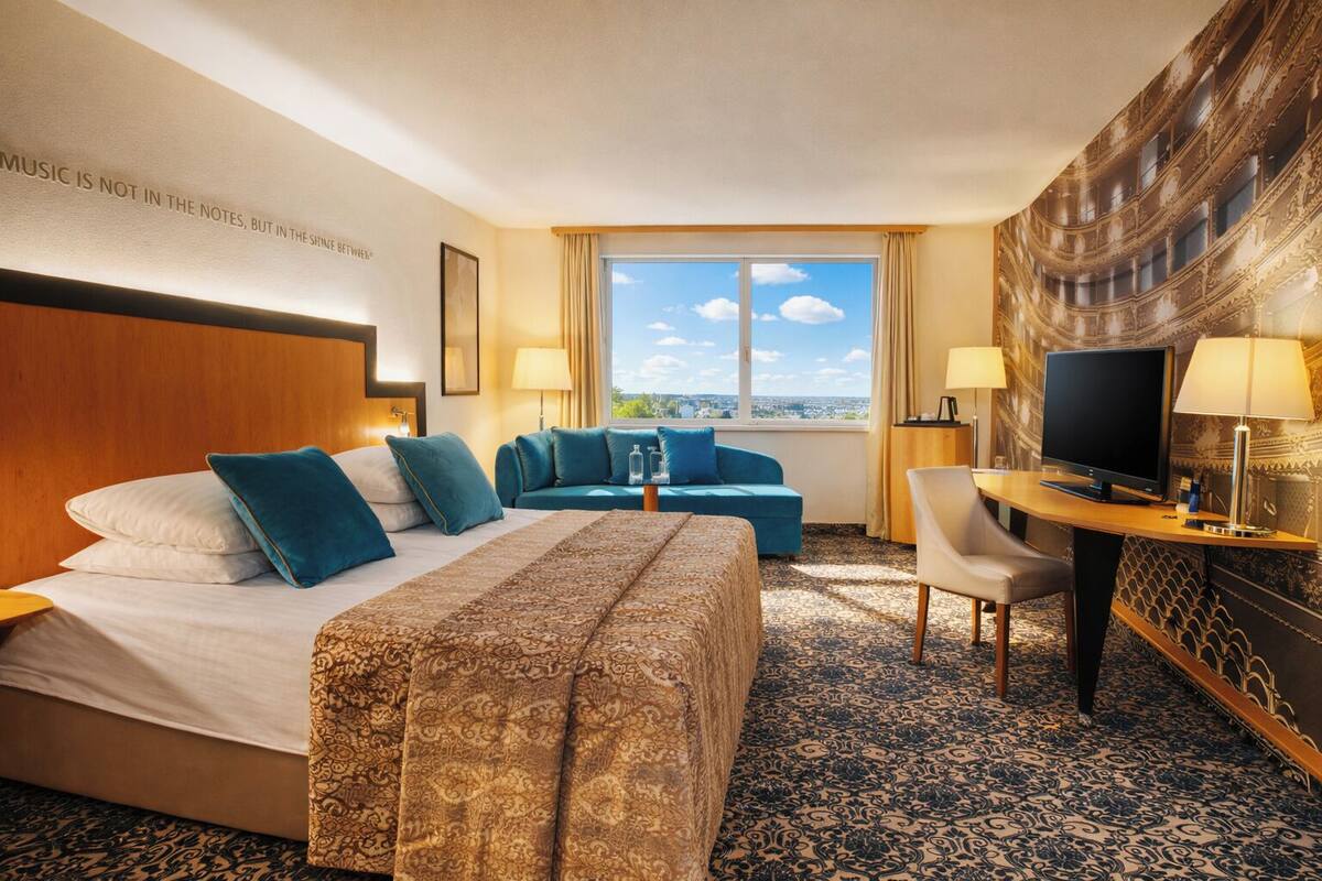 A hotel room with a bed, two sofas, a desk with a TV, and a large window with a city view.