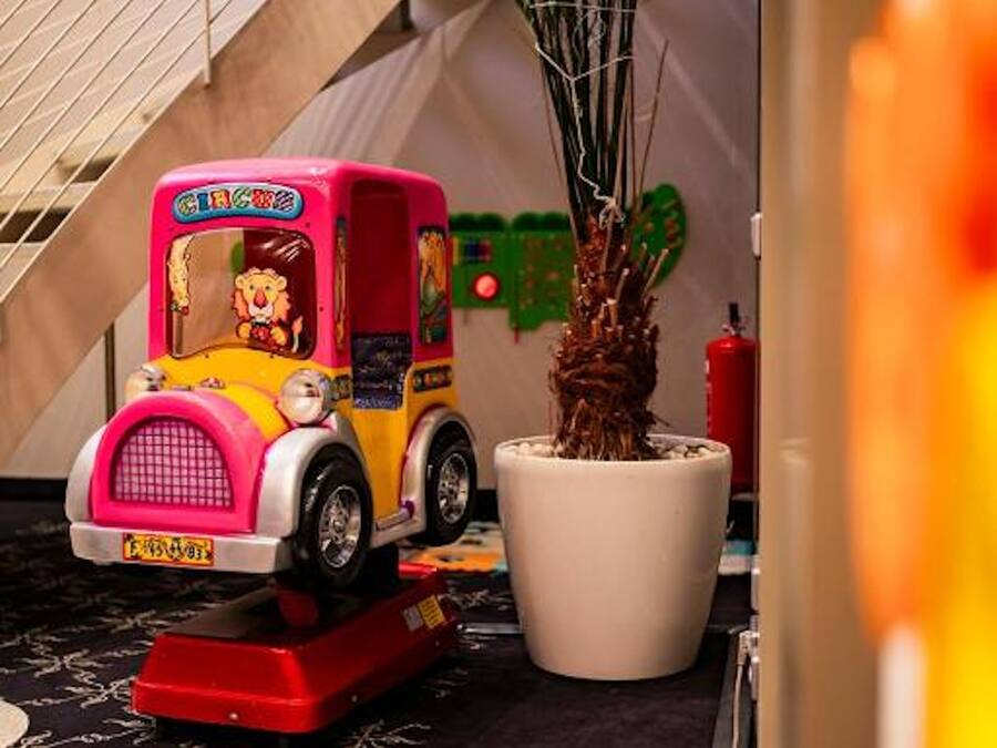A toy car with a lion on the front, a large potted plant, and a tent-like structure in the background.