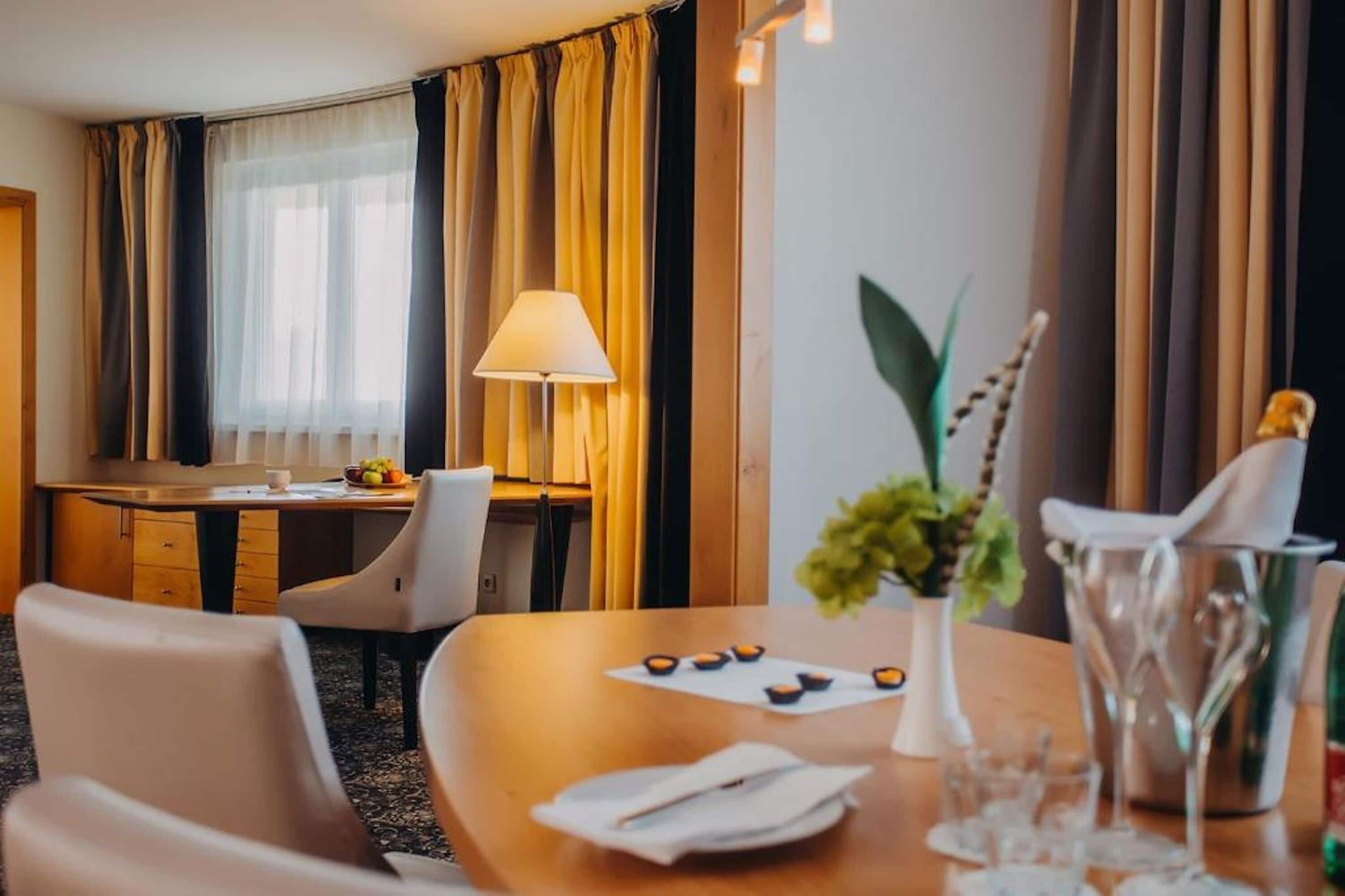 Ein Hotelzimmer mit Essbereich, ausgestattet mit einem Holztisch, Stühlen, einer Blumenvase und einer Lampe.