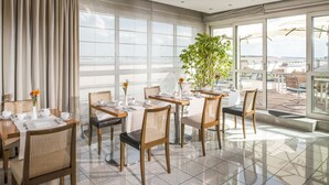 Zona pranzo moderna con ampie finestre, una pianta e vista sulla città.