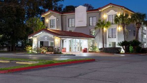 A two-story hotel with a red-tiled roof, a covered entrance, and a landscaped front yard with palm trees.