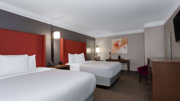 A hotel room with two beds, a desk, a chair, a lamp, and a painting on the wall.